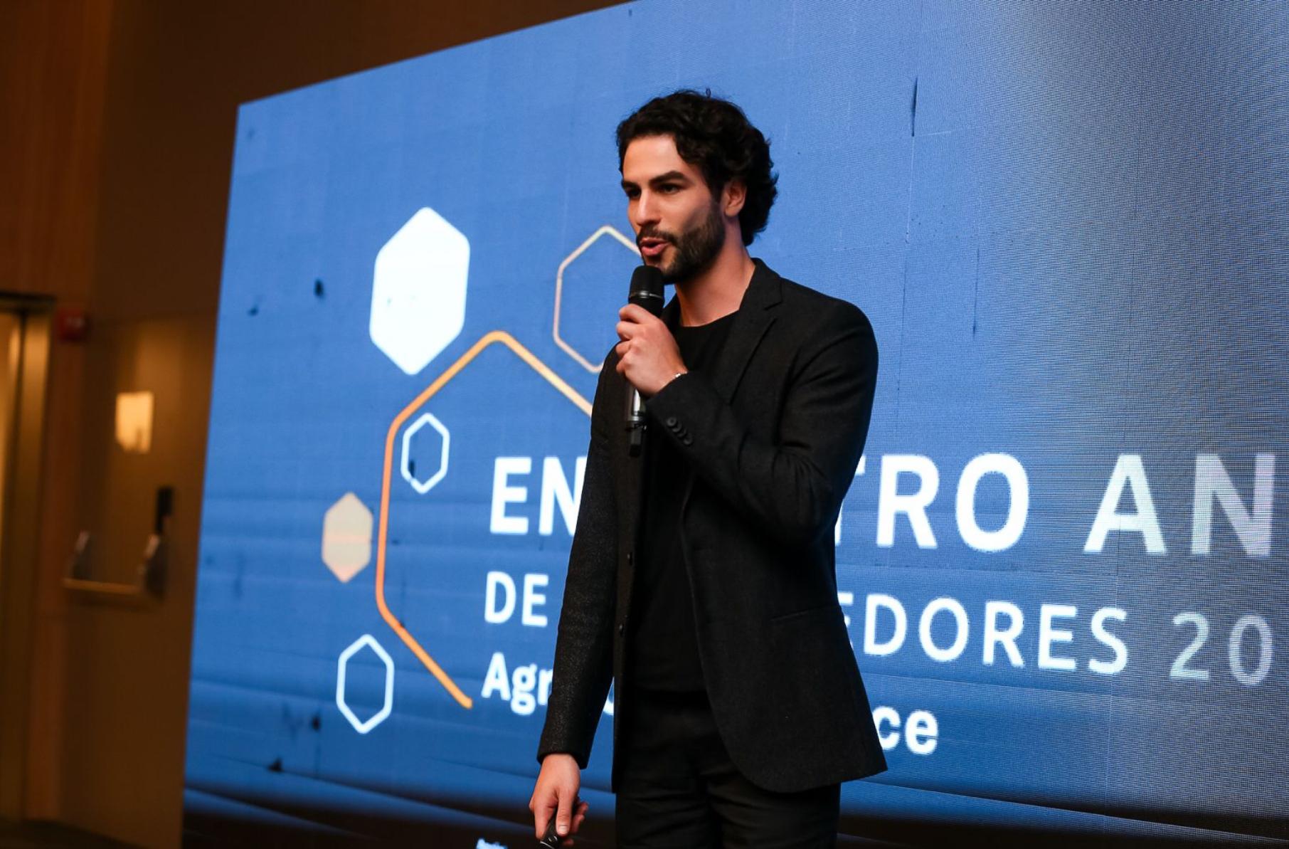 Na foto temos um homem de preto discursando na frente de um painel. O homem da foto é Felipe Muniz , co-fundador da HiSolver/ Foto usada como ilustração da matéria: HiSolver: conheça plataforma que usa IA para democratizar o aprendizado