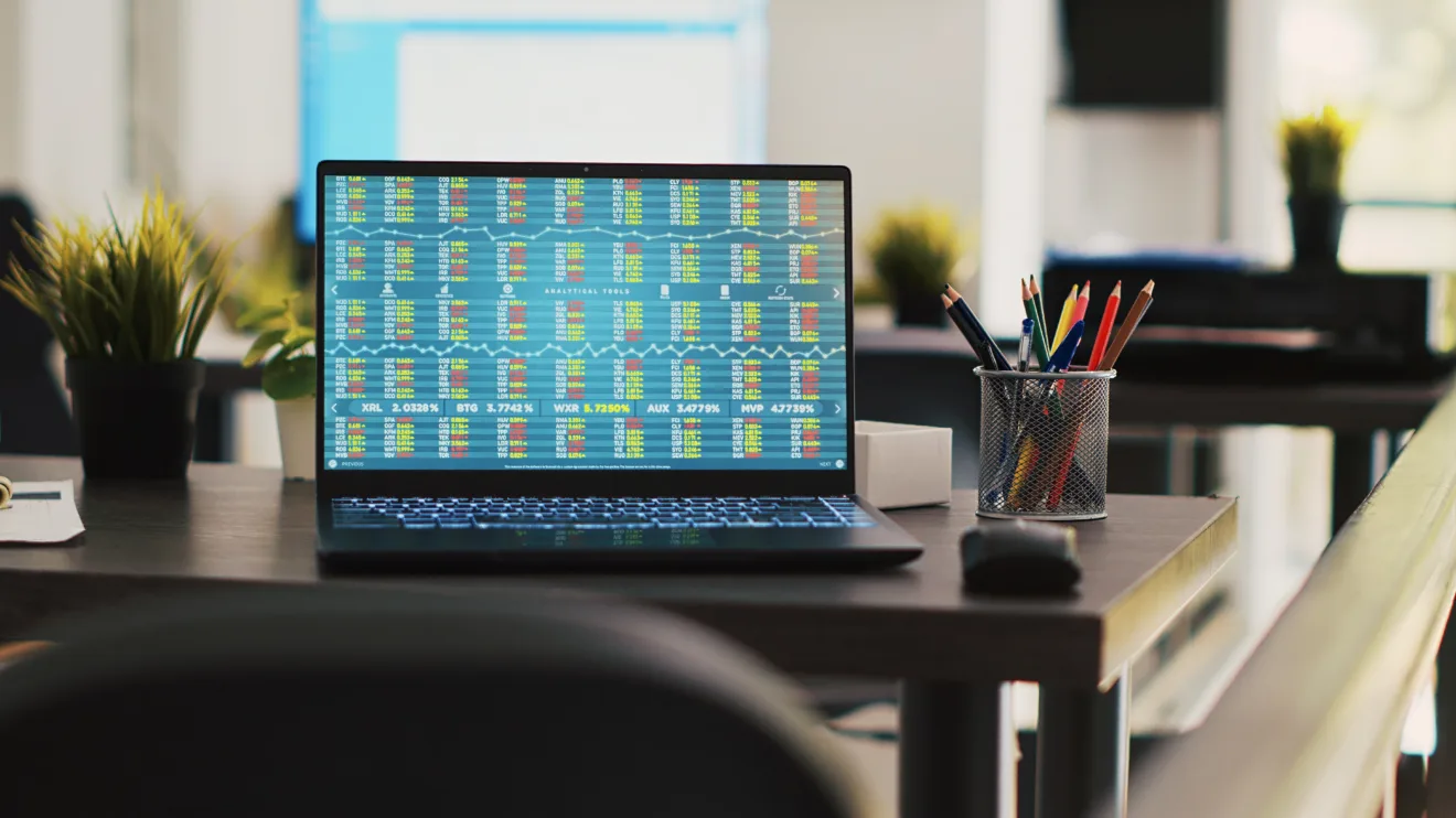 Company documents and laptop in financial department office showing stock exchange values. Business files on desk next to notebook showing forex trading indexes prices, handheld camera shot