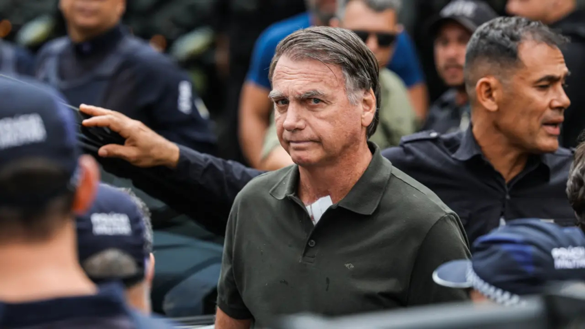Foto de Bolsonaro, ex-presidente do Brasil, com uma roupa escura, em meio a vários seguranças.