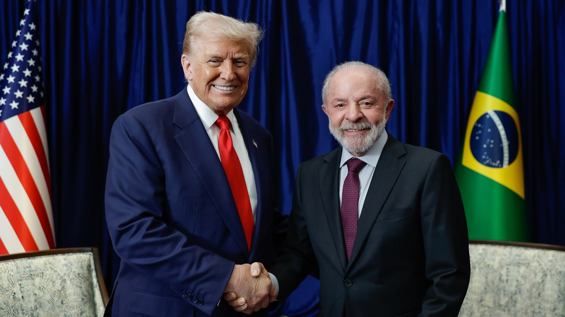 Presidente Lula e Trump de mãos dadas ao fundo as bandeiras de Brasil e EUA
