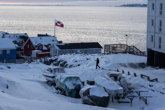 Uma bandeira da Groenlândia tremula enquanto um homem caminha no dia do encontro entre altos funcionários dos EUA e os ministros das Relações Exteriores da Dinamarca e da Groenlândia, em Nuuk, Groenlândia, 14 de janeiro de 2026.