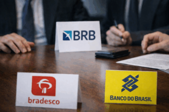 Imagem horizontal realista mostrando uma mesa de reunião com placas dos bancos BRB, Banco do Brasil e Bradesco, enquanto executivos negociam ao fundo. A cena representa a discussão para venda de carteira de crédito entre instituições financeiras, ilustrando reportagens sobre operações estratégicas no setor bancário brasileiro. Composição limpa, iluminação corporativa e foco nos logos reforçam o contexto financeiro.