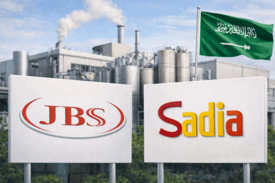 Imagem horizontal realista mostrando a fachada de uma fábrica moderna de processamento de alimentos na Arábia Saudita, com placas exibindo os logotipos da JBS e da Sadia em primeiro plano. Ao fundo, estrutura industrial metálica e a bandeira da Arábia Saudita levemente desfocada, representando a expansão internacional da JBS e a concorrência no mercado global de alimentos.